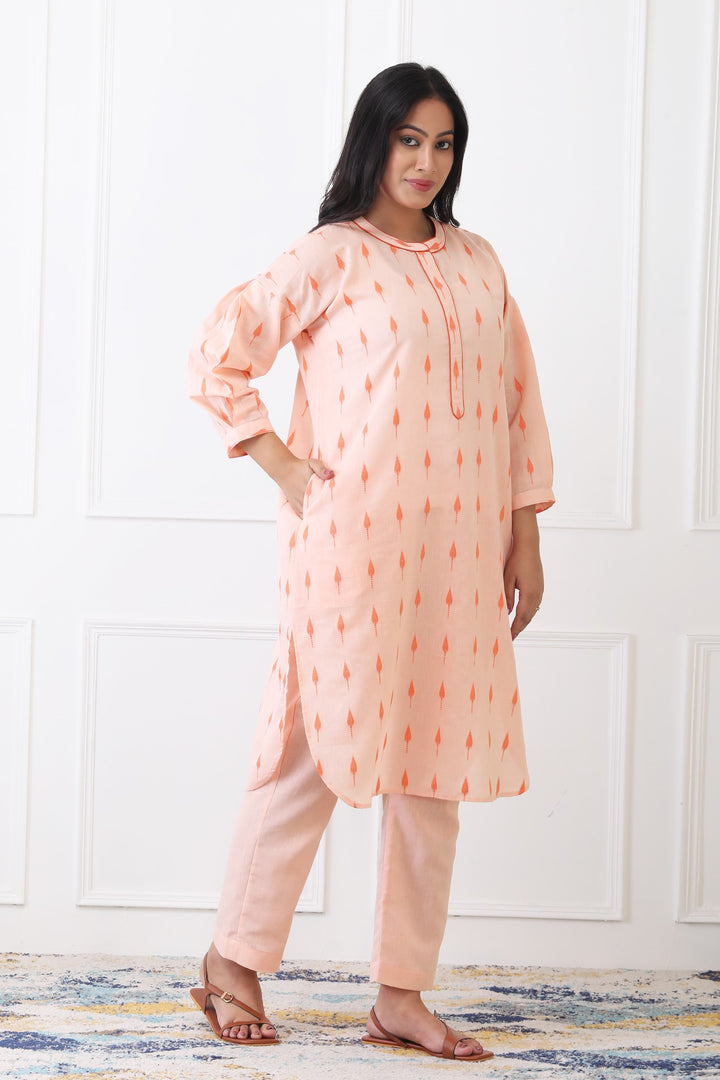 Woman wearing a peach-colored kurta with white pants against a white wall.