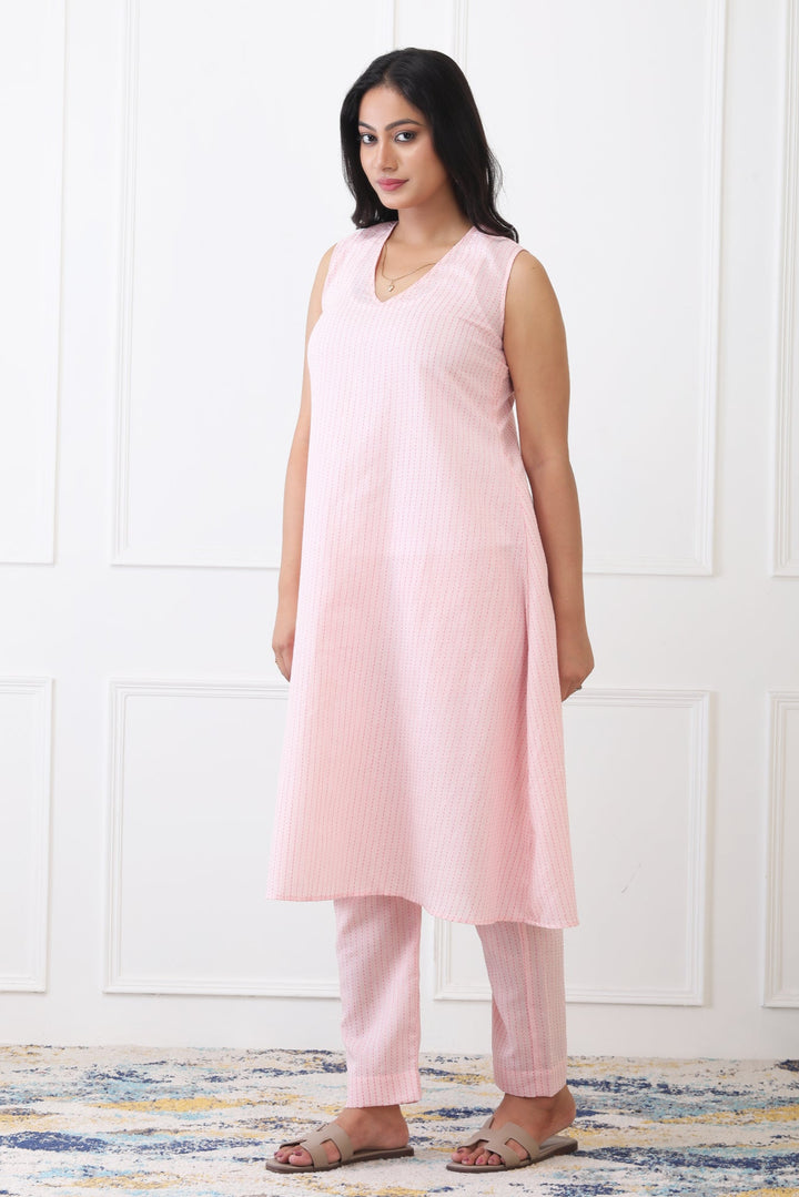 Woman wearing a pink sleeveless top and pants against a white wall.