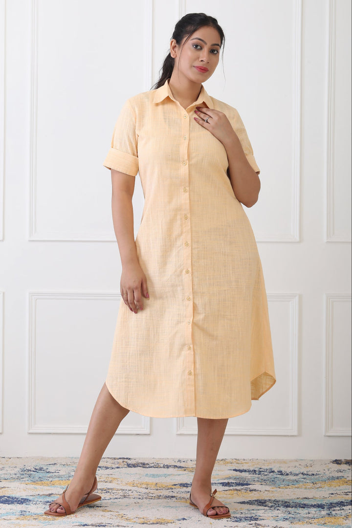Woman wearing a yellow dress standing against a white paneled wall.