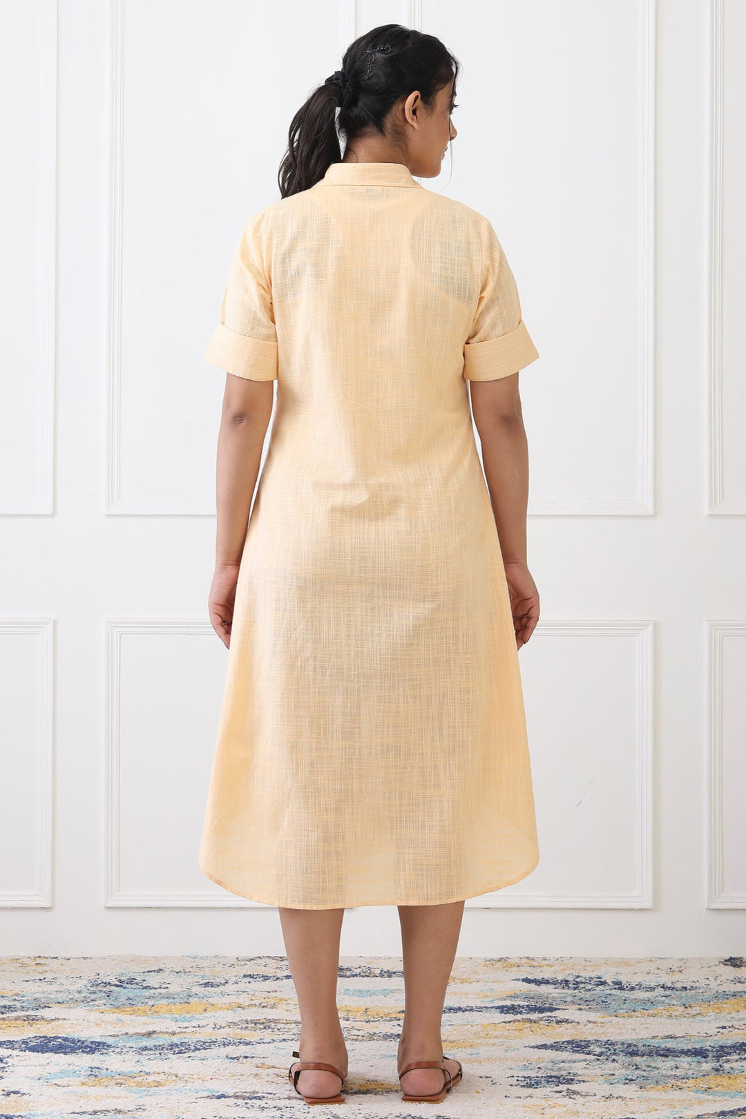 Woman wearing a beige dress standing against a white paneled wall.