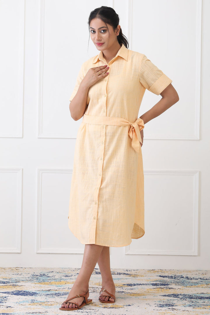 Woman wearing a yellow dress standing in a room with white walls and a patterned rug.
