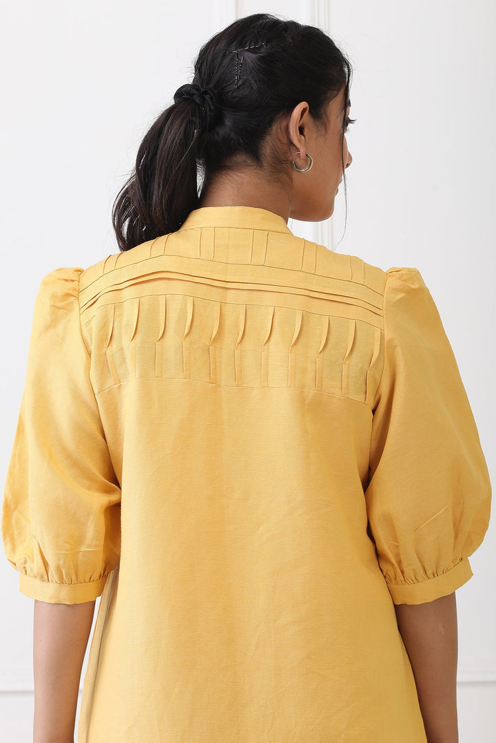 Woman wearing a yellow dress with puffed sleeves against a white background