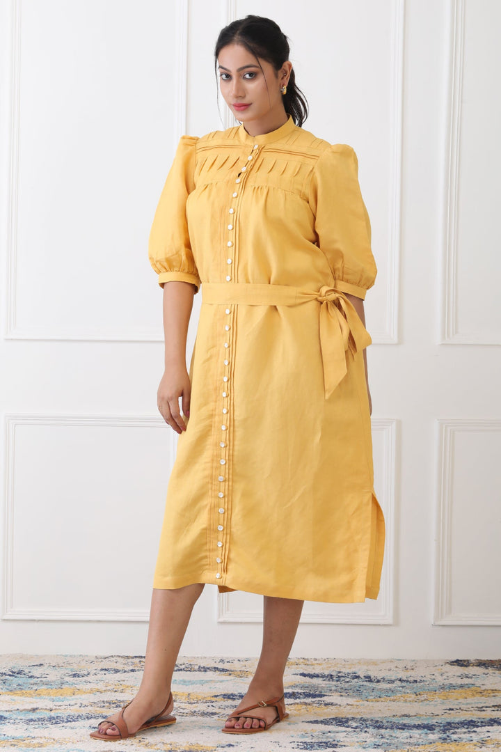 Woman wearing a yellow dress standing against a white wall.
