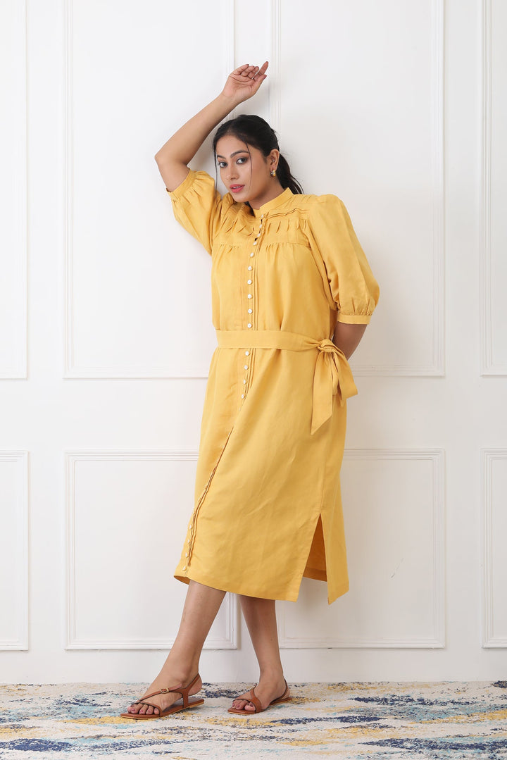 Woman wearing a yellow dress standing against a white wall.