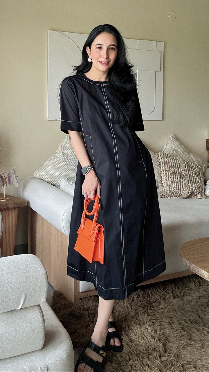 Woman in a black dress standing in a modern living room with a white sofa and round chair.