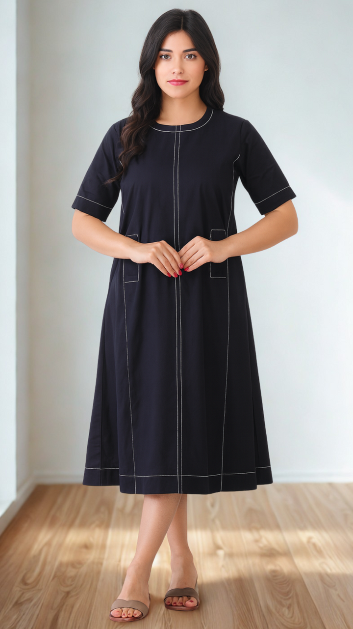 Woman wearing a black dress with white piping standing in a room with wooden flooring.