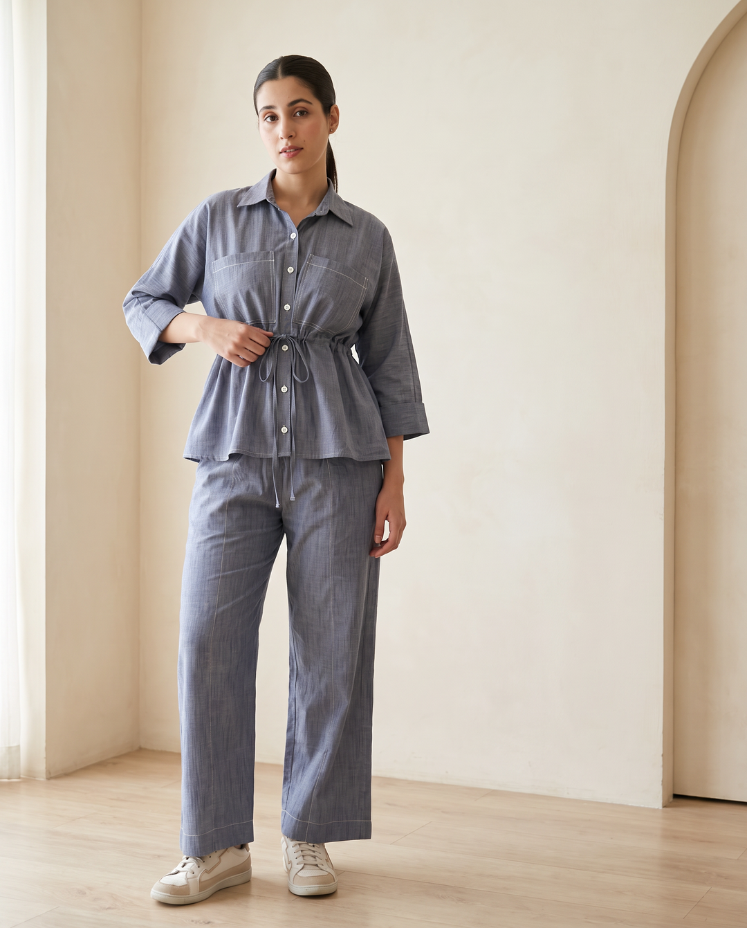 Woman wearing the Alexis blue-grey denim chambray co-ord set: shirt with drawstring waist and wide-leg trousers, front view