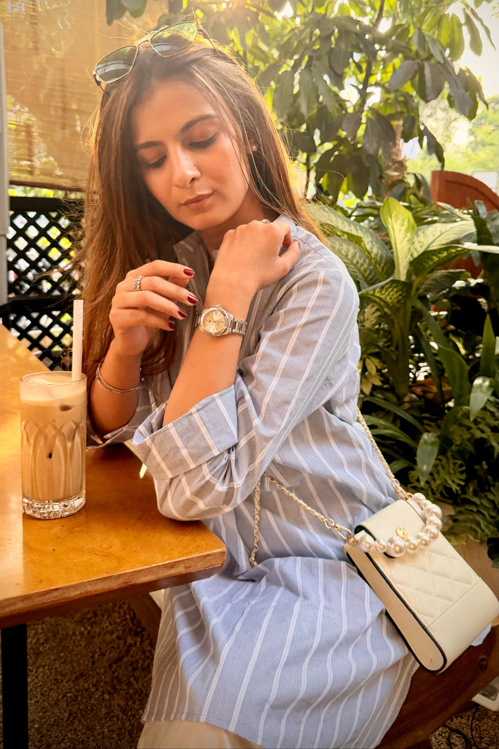 Woman sitting at a table in an outdoor cafe, wearing a striped shirt and a watch.