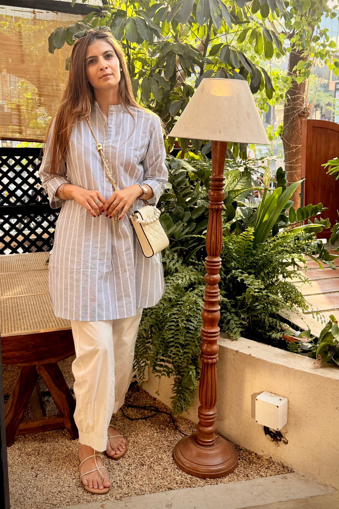 Woman standing in a garden setting with plants and a lamp.